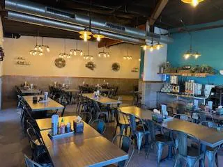 Hanoi-Chicken-Noodle-Vietnamese-Restaurant-San-Leandro A spacious restaurant interior with wooden tables, metal chairs, pendant lighting, and a teal accent wall featuring decorative plates.